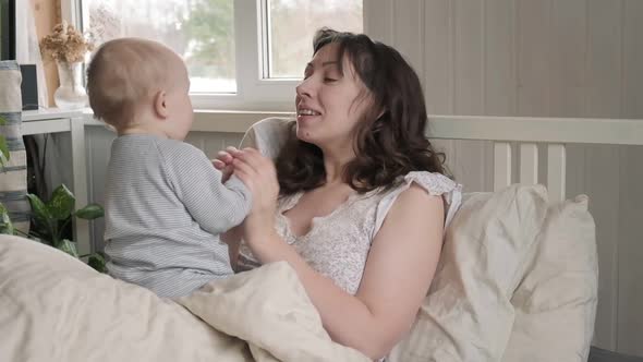 Mother in Nightwear Waking Up with Her Tiny Newborn Playing on Bed alt