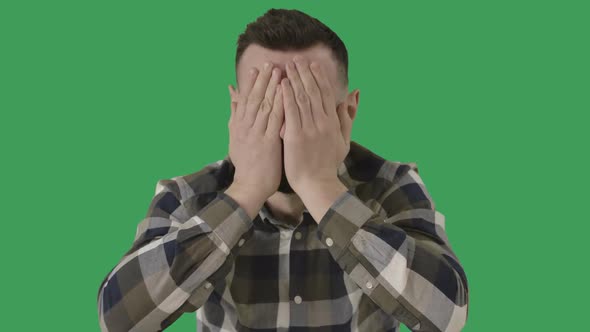 Portrait of Crying Caucasian Handsome Man at Green Screen Background. Brunette Depressed Guy Rubbing alt