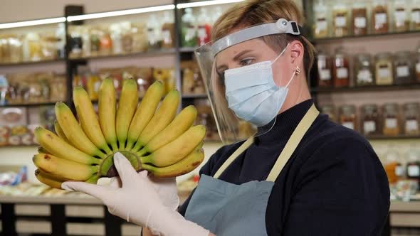 Closeup of a Salesman in a Mask Holding Small Bananas in a Grocery Store alt