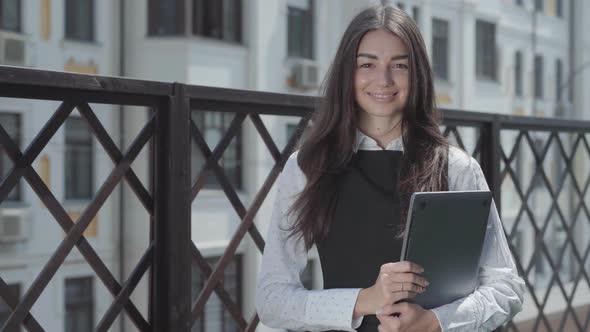 Portrait of a Pretty Young Woman on the Terrace Looking in the Camera Holding Laptop in Hands alt