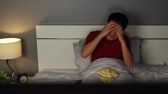 sad young man watching sport TV and lose a game on a bed at night