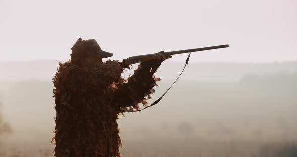 Portrait of hunter in hunting equipment. Silhouette of man in sunset light find the target and aims alt