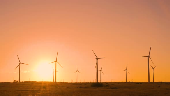 Spinning Wind Turbines in Field Against Big Sun at Sunset with Warm Orange Sky. Eco Energy Concept alt