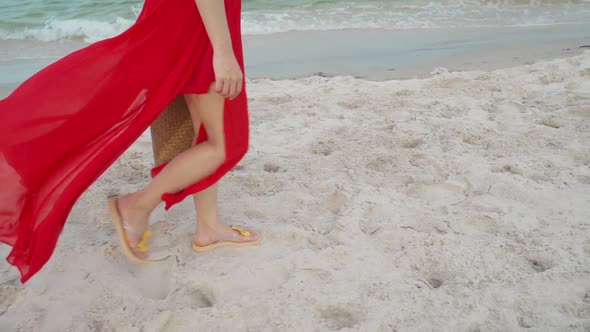 slow-motion of woman feet in red dress walking on the sea beach with wind blow alt