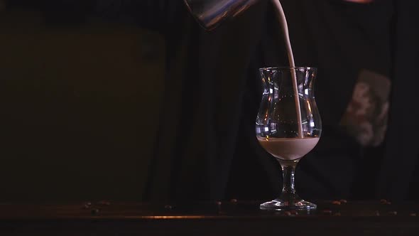 In a Dark Room Close-up the Bartender Pours Coffee with Milk Into a Transparent Glass