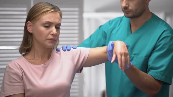 Surgeon Examining Sad Patient Shoulder After Trauma, Raising Female Hand, Rehab