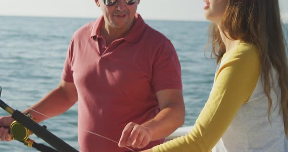 Side view of a Caucasian man and his teenage daughter fishing on boat alt