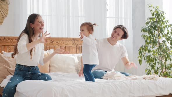 Family Having Fun at Home Bedroom in Morning Little Girl Toddler Dancing to Music on Bed Father and alt