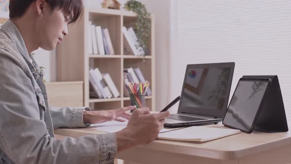 Asian designer man uses his smartphone to communicate. Work on projects and papers. and work from ho alt