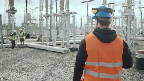 Geodesist in Helmet and Vest Holds Pole at Electric Station