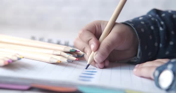 Close Up of a Child Hand Drawing with Colored Pencil on a Page alt