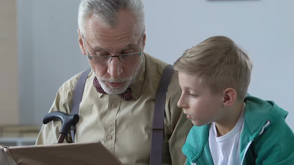 Male Pensioner Reading Story Book for Grandson, Explaining School Subject, Help alt