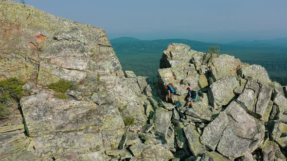 Aerial Couple of Hikers Climbing Rocky Cliff Slope to the Mountain Peak