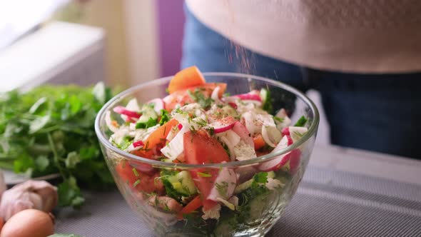 Woman Adding Salt and Spices Into Mixed Salad of Vegetables  Tomatoes Cucumbers Onion Parsley alt