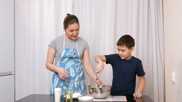 Boy Beats Eggs with a Whisk Under the Supervision of a Woman in the Kitchen alt