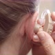 A woman puts a hearing aid on her ear. Deafness. - VideoHive Item for Sale