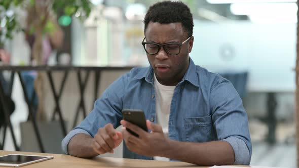 Upset Young African Man Reacting to Loss on Smartphone alt