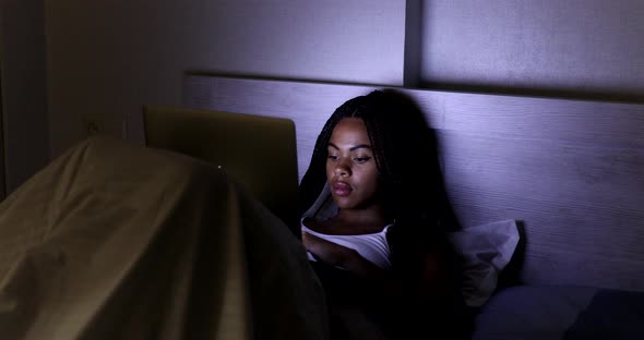 Happy pretty black woman using laptop on bed.
