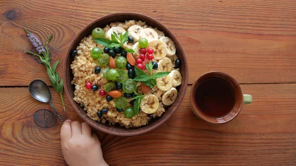 Wholegrain Oatmeal porridge with fresh berries, fruits, nuts, mint leaves in child hands alt