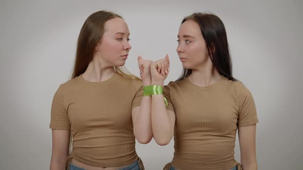Twins with Serious Facial Expression Posing at Grey Background with Tied Hands alt