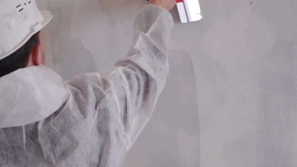 A Man in a Hard Hat Aligns the Walls with a Spatula and Plaster