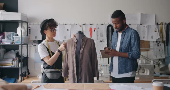 Man and Girl Tailors Measuring Clothes on Dummy Writing Measurements in Notebook alt