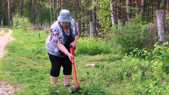 An Elderly Woman Mows Low Green Grass with an Electric Trimmer alt