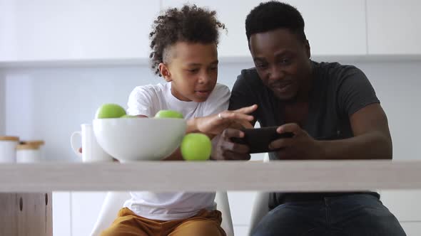 Front View of Young Father and Son Using Smartphone at Table in Apartment Interior Spbi alt
