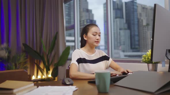 Asian woman sitting at home working at her desk with documents and computer alt