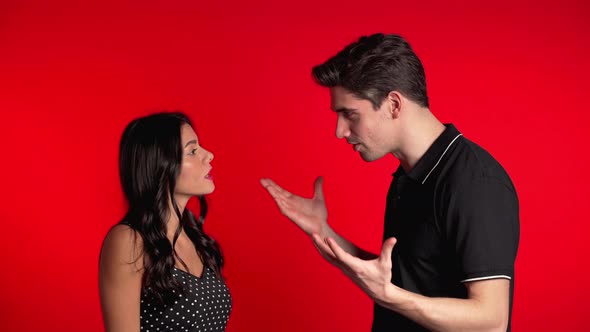 Young Couple Emotionally Quarreling on Red Background in Studio.  alt