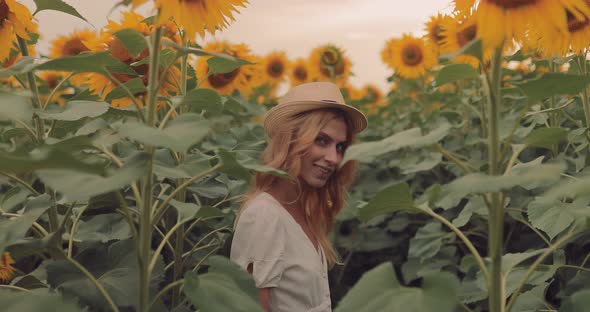 Pretty Girl in a Hat Runs Away in a Field of Sunflowers and Laughs