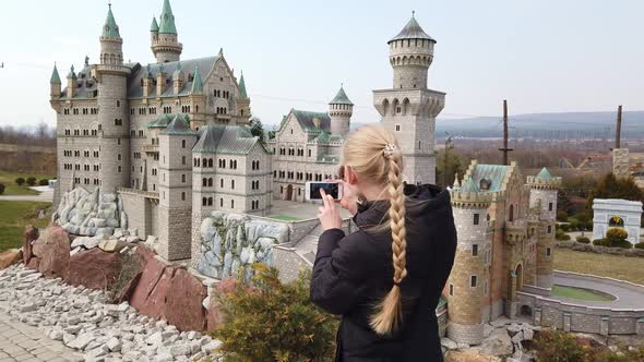 Woman Makes Photo Walking on Foot Near a Miniature Model of the Old Castle Neuschwanstein, Germany alt