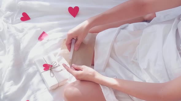 A Woman in a White Bed Opens an Envelope and Takes Out a Greeting Valentine Card for Valentine's Day