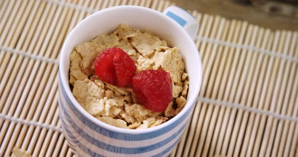 Flakes with raspberries in mug on place mat 4k alt