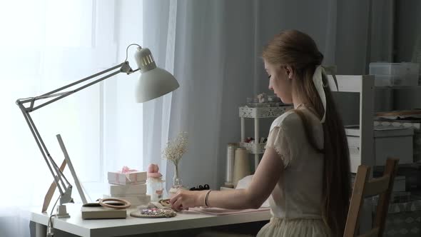 Young designer girl creates beautiful jewelry and embroider patterns on the fabric alt