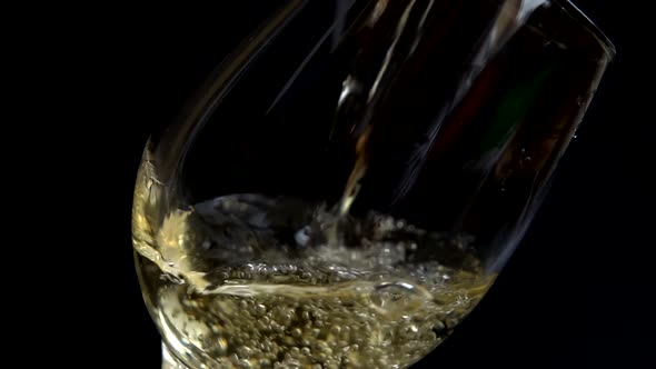 Wine is poured into a glass on a black background. Slow motion. alt