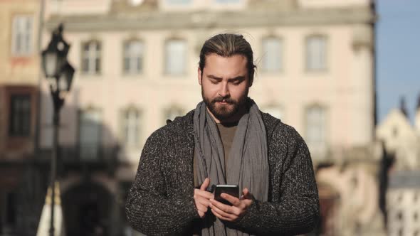 A Bearded Man is Browsing Social Networks on a Smartphone and Raising His Head alt