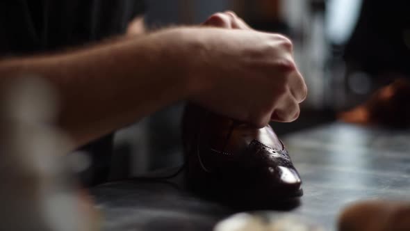 Tracking shot of male shoemaker tying laces on repaired and polished light brown leather shoes. alt