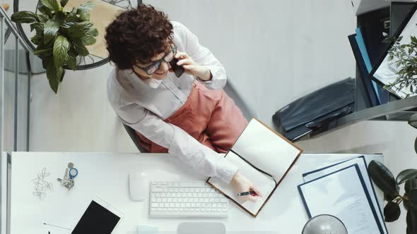 Top Down of Business Lady Talking on Phone and Taking Notes in Office alt