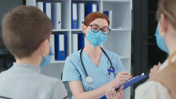 Family From Back at Doctor Consultation Pediatrician in Protective Mask Writes Notes on a Clipboard alt