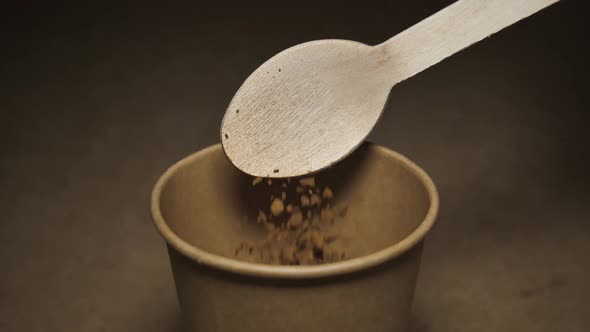 Coffee Falls From a Wooden Spoon Into a Paper Craft Glass on a Gray Background alt