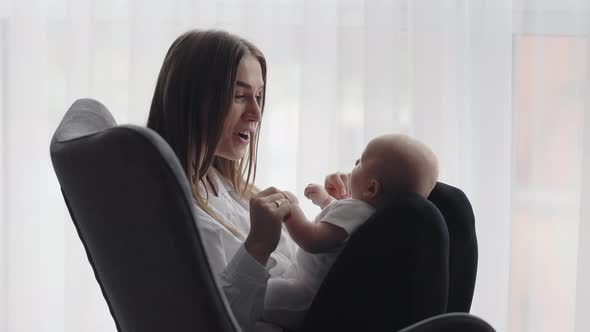 Charming Woman Sitting in Chair and Playing with Toddler alt