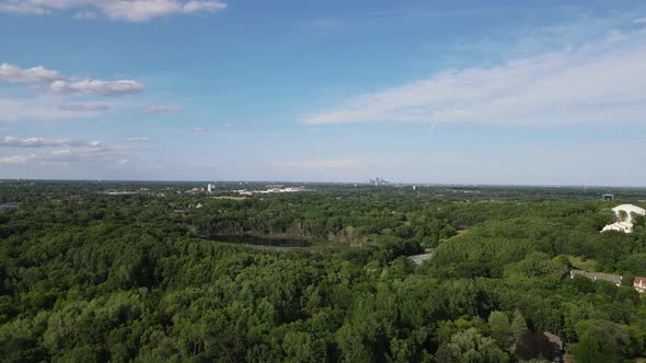 Drone view over outside Minneapolis with extensive green foliage and small lake. Blue sky.