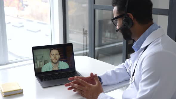 Indian Male Doctor Using Laptop for Online Meeting with Patient Listens to Complaints alt