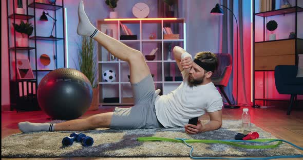 Man in Sportswear Lying on the Floor in the Evening and Doing Leg lifts Exercises alt