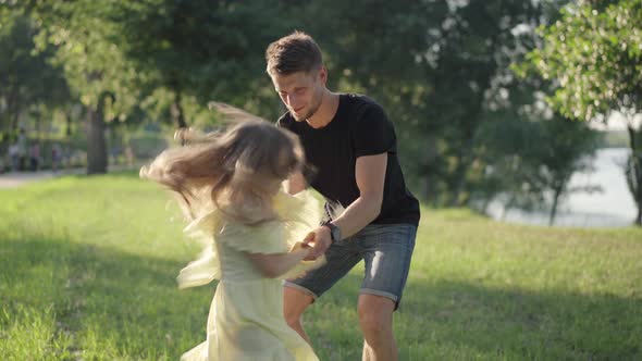 Playful Girl in Yellow Dress Having Fun with Young Smiling Man in Sunny Park alt