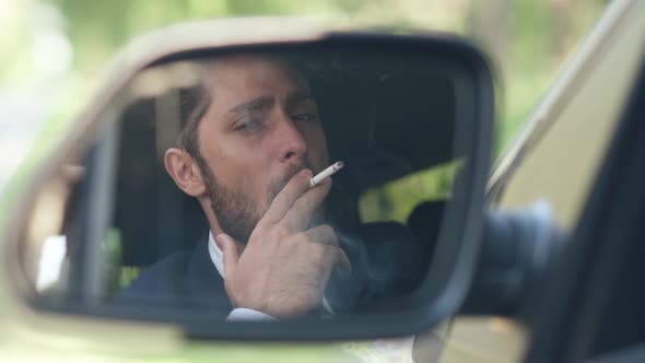 Reflection in Side View Mirror of Young Caucasian Man Smoking Cigarette Sitting on Driver's Seat in alt