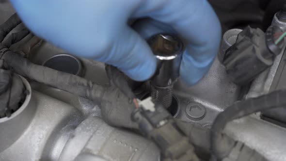 Hands in Protective Gloves Inserting and Screwing in New Spark Plug with Socket Wrench in Engine Bay