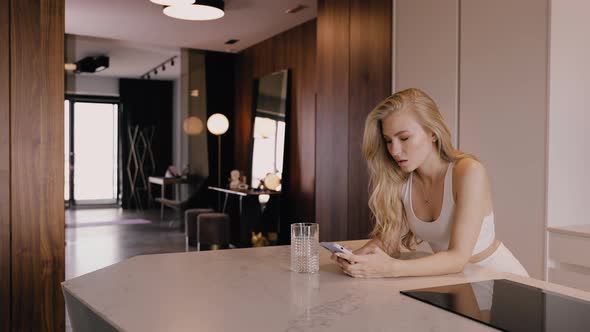 A Young Blonde with a Phone in Her Hands is Chatting Intently By the Phone alt