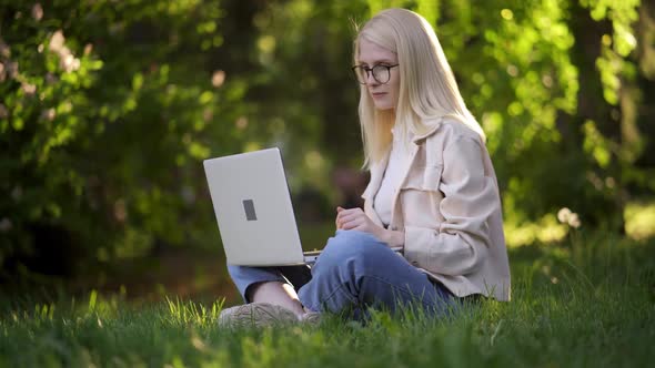 Happy Woman Student Sitting on Green Grass with Laptop in the Park alt